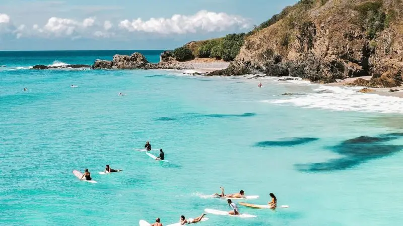 A group of surfers with boards relaxes on clear turquoise water during The Great Escape Australia 28 Day Semi-Guided adventure tour.