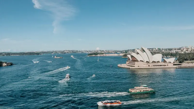 Iconic Sydney Opera House overlooking sparkling blue harbour waters with boats, launch point for The Great Escape Australia 28 Day tour.