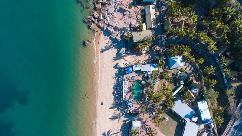 Stunning aerial shot of pristine sandy beach with crystal-clear turquoise waters and lush palm trees on The Great Escape Australia tour.