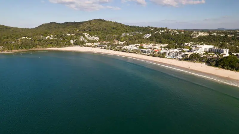 Stunning aerial view of a pristine curved beach with turquoise waters and lush green hills on The Great Escape Australia 28 Day tour.