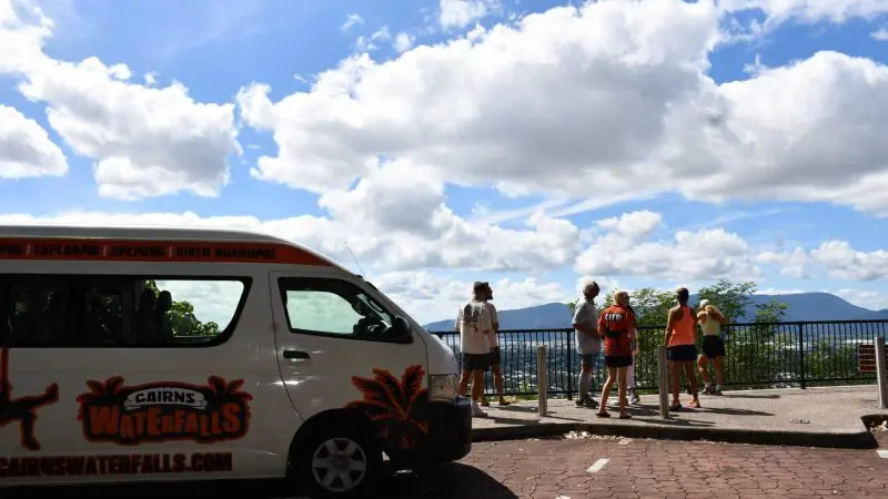 Creek To Coral Mission Beach Day Tour van at a stunning viewpoint where travellers admire mountain views beneath dramatic, cloudy skies.