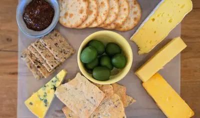 Luxurious cheese board featuring artisan crackers, green olives, three premium cheeses, and a bowl of gourmet chutney or jam.