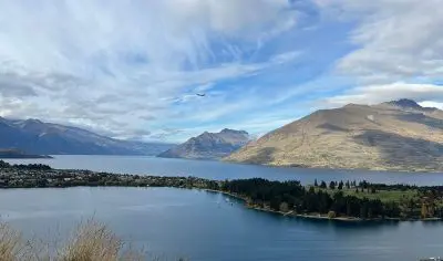 Stunning aerial view of Queenstown’s crystal-clear lake, encircled by majestic mountains and charming town—ultimate travel highlight.