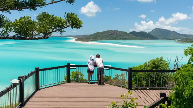 Couple enjoys stunning turquoise waters and scenic islands from a deck on a luxury Purely Whitehaven Day Tour in the Whitsundays.