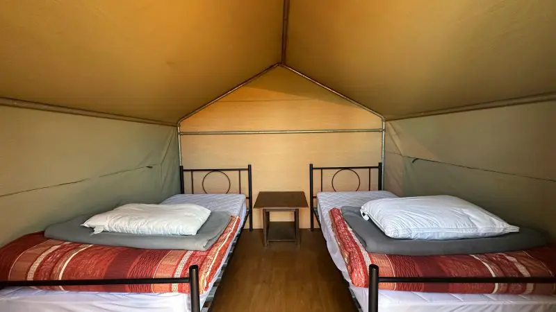 Spacious canvas tent with two single beds, plump pillows, and cosy blankets—ideal accommodation for an Uluru Red Centre family adventure.