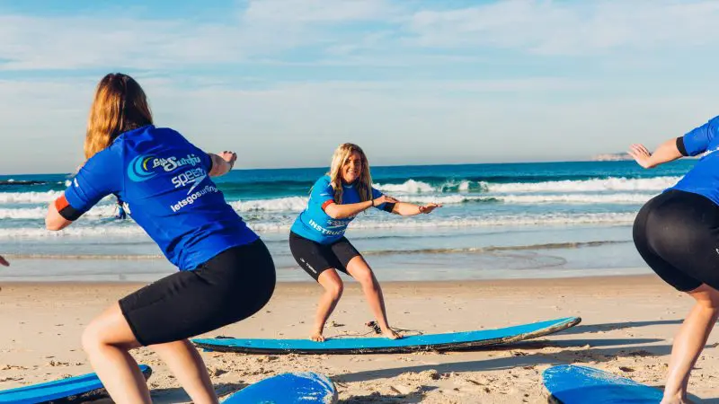 Children in matching blue shirts learn to surf on sandy Byron Bay beach—top-rated group surfing lessons for children, book now.