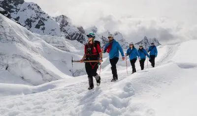 Five adventurers in winter gear trek across Franz Josef Glacier, framed by dramatic snow-capped peaks on a guided glacier hiking tour.
