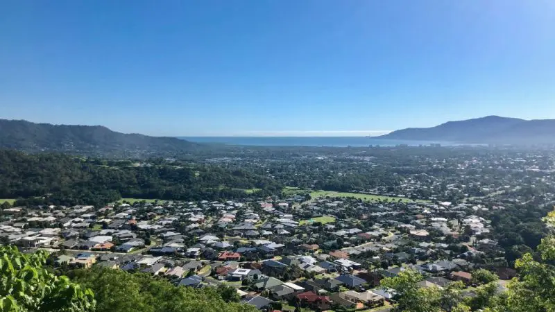 Stunning aerial view of Cairns City, showcasing suburban neighbourhoods, lush mountains, and the Coral Sea by Green Island under clear skies.
