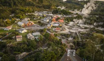 Aerial photo of Whakarewarewa village, showcasing active geothermal vents with steam, lush green hills, and native New Zealand trees.