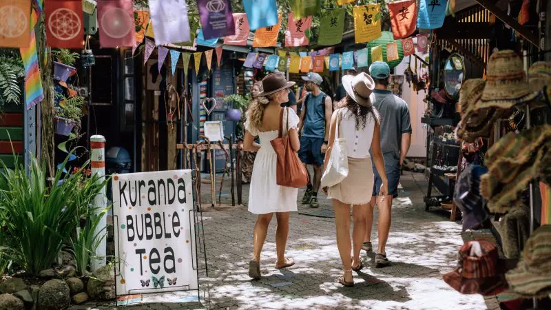 Three travellers enjoy Kuranda Bubble Tea whilst exploring a lively Australian market on the 16 Day Best of East Coast Comfort Tour.