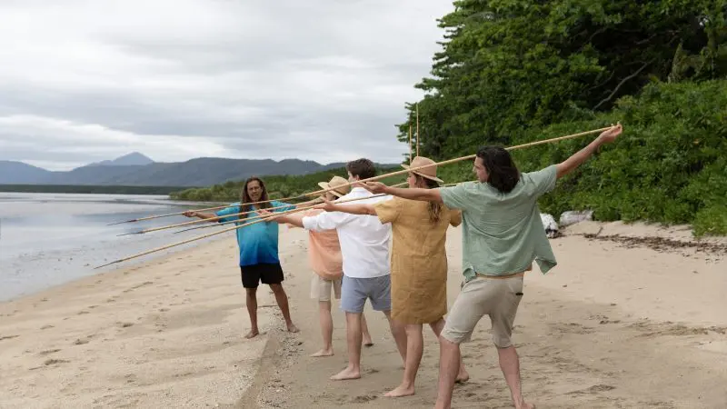 Small group practises traditional spear throwing on a pristine sandy beach during the 3 Day Daintree Cape Tribulation Port Douglas Tour.
