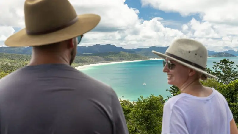 Two travellers in sun hats admire a breathtaking bay view—ideal for a 14 Day Sydney to Cairns with Fraser Island Whitsundays Comfort Tour.