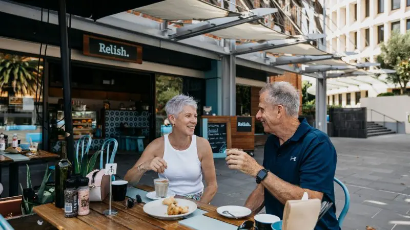 Senior couple sipping coffee at Relish café, fondly recalling their 14 Day Sydney to Cairns Comfort Tour adventure together.