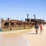 Couple walks by a rusty shipwreck during a 14-Day Sydney to Cairns tour with stops at Fraser Island and Whitsundays, Australia.