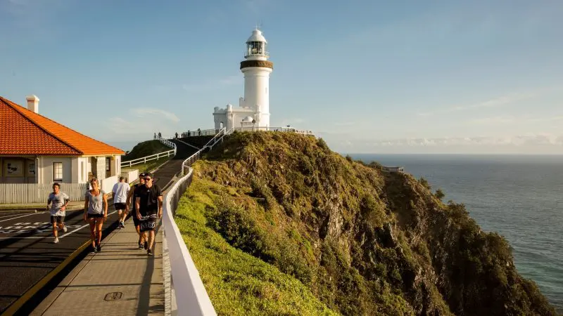 Travellers stroll a scenic path towards a striking white lighthouse, highlight of the 16 Day Best Of East Coast Australia Comfort Tour.