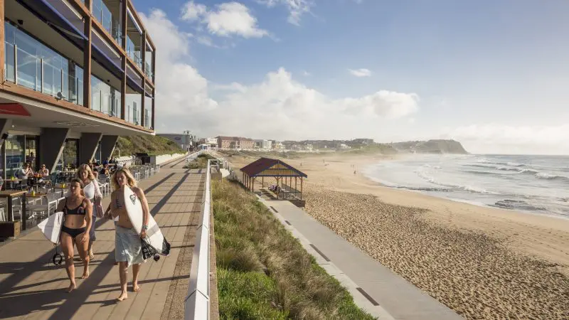 Surfers stroll along a scenic seafront promenade under clear skies during the 8 Day Sydney to Brisbane with Fraser Island Comfort Tour.