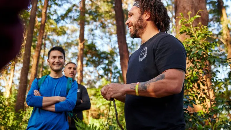 Three men smiling in a sun-drenched forest during their 8-Day Sydney to Brisbane with Fraser Island Comfort Tour adventure.