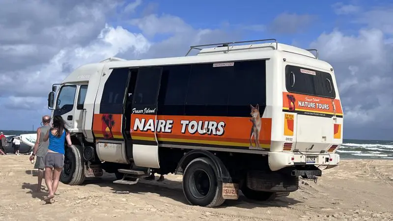 8 Day Sydney to Brisbane with Fraser Island Comfort Tour coach parked on pristine sandy beach by the sea, perfect coastal adventure.