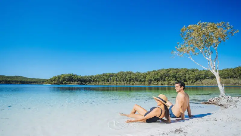 A couple enjoys a sunny sandy beach and crystal-clear blue water on the 8 Day Sydney to Brisbane with Fraser Island Comfort Tour.