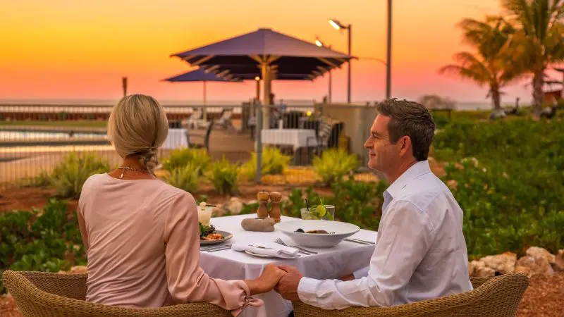 Couple enjoying romantic outdoor dining at sunset on their 8 Day Perth to Exmouth Comfort Tour, with stunning coastal scenery.
