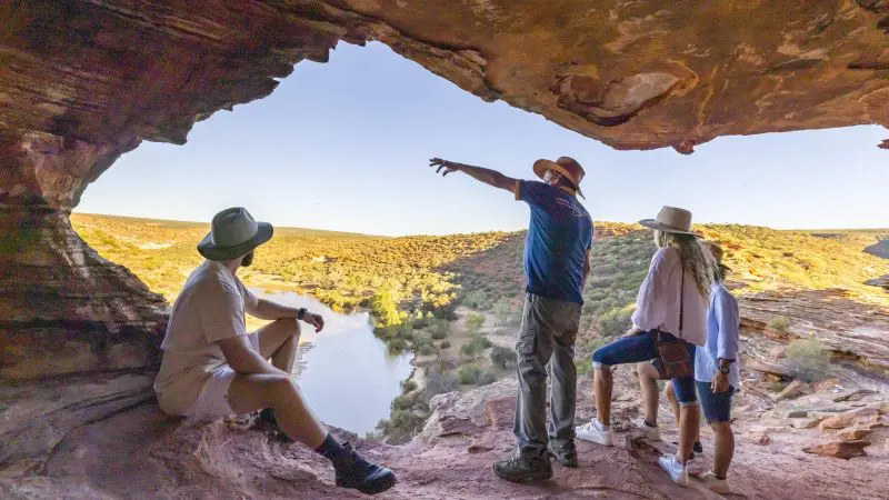 Three travellers in hats admire a scenic river from a rocky cave on the Perth to Exmouth Comfort Tour, exploring coastal wonders.