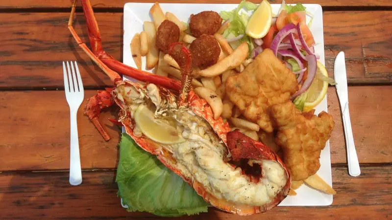 Seafood platter with succulent grilled rock lobster, crispy fried fish, golden chips, hush puppies, fresh salad, and lemon wedges.