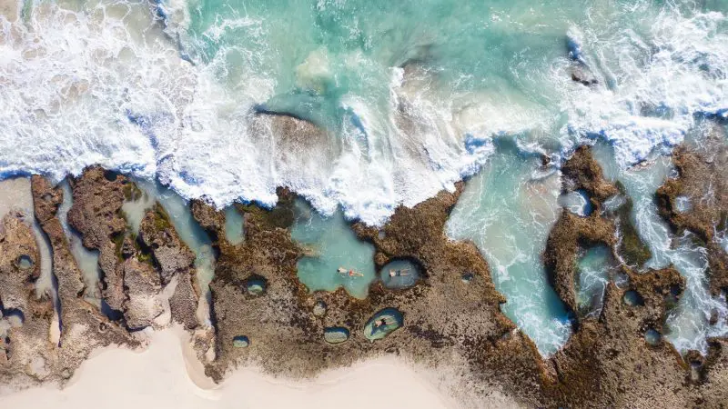 Stunning aerial view of turquoise waves over rocky tide pools by Ningaloo Reef, featured on the 8 Day Perth to Exmouth Comfort Tour.