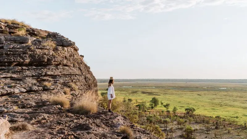 Traveller in white standing atop a rugged cliff, overlooking lush green plains—ideal for an unforgettable 1 Day Kakadu Wilderness tour.