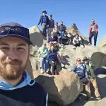 A smiling group on rugged rocks beneath a clear sky captures a selfie during their Kangaroo Island 2 Day Wildlife Adventure tour.