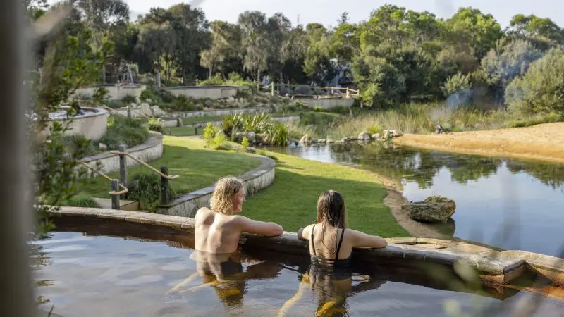 Two people unwind in a natural hot spring pool after a Peninsula Hot Springs Spa day tour with shuttle bus, enjoying ultimate relaxation.
