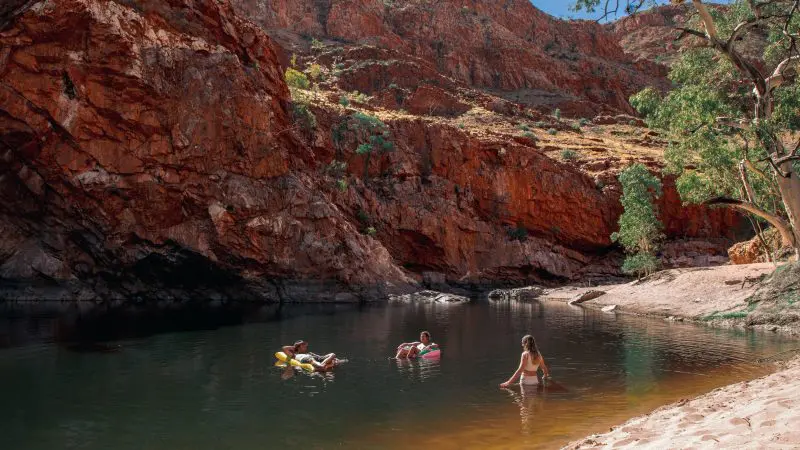 Visitors swimming and unwinding in a pristine waterhole during a 1 Day West MacDonnell Ranges and Standley Chasm tour adventure.