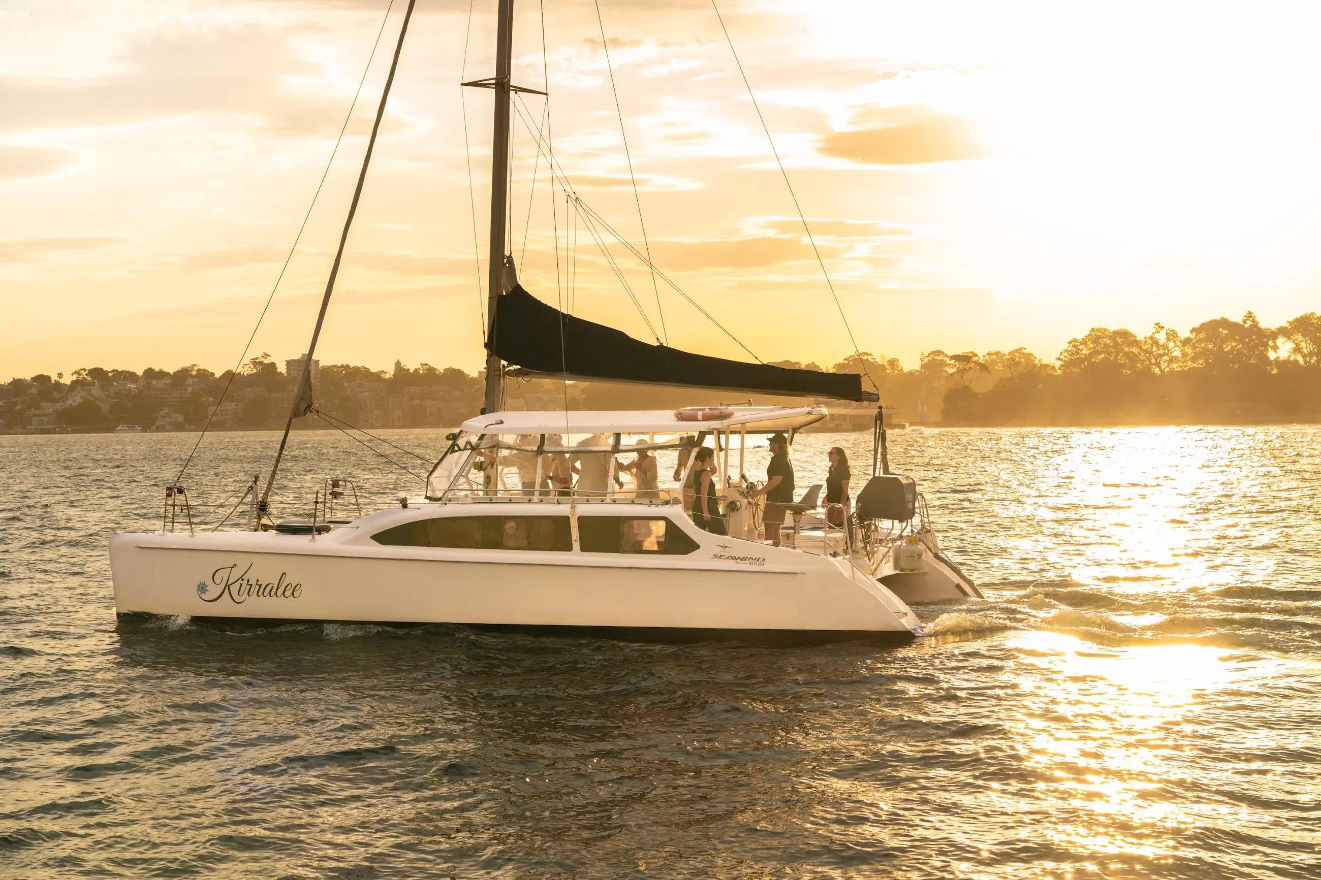 A white catamaran glides at sunset on Sydney Harbour as guests enjoy a BYO Sparkle Cruise, with iconic city views in the background.