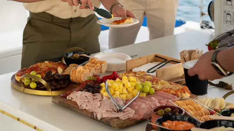 Guests savour a gourmet charcuterie board aboard a Sydney Harbour BYO Sunset Sparkle Catamaran Cruise with stunning waterfront views.