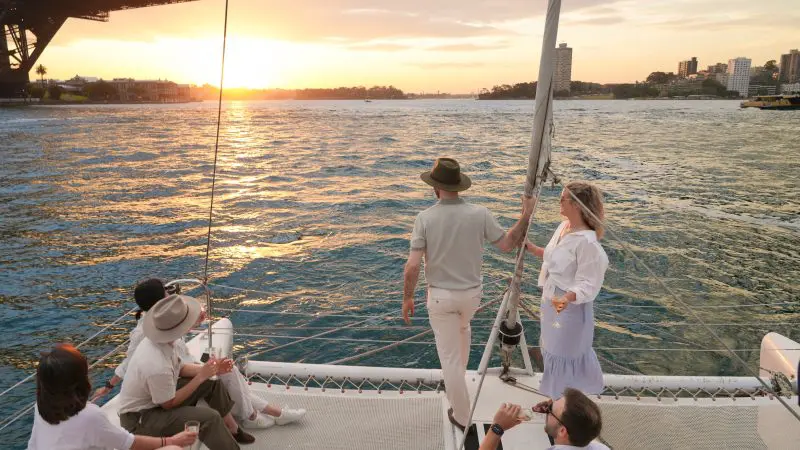 Group of five unwind on a Sydney Harbour BYO Sparkle Catamaran Cruise at sunset, with iconic skyline and Harbour Bridge views.