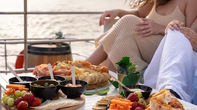 Gourmet table with assorted fruit, premium cheeses, and snacks on a luxury boat at sunset during Sydney Harbour Golden Glow Cruise.