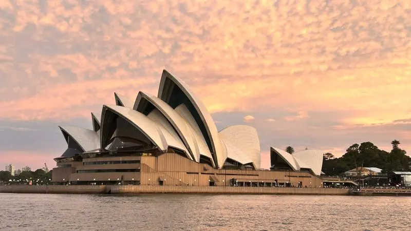Iconic Sydney Opera House silhouetted at sunset with vibrant pink clouds, viewed on a Sydney Harbour Golden Glow Sunset Cruise.
