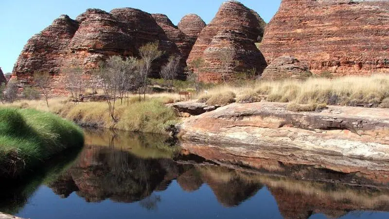 Striking layered red rock formations and lush green banks mirrored in a tranquil pool on your 10 Day Darwin to Broome 4WD tour.