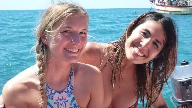 Two young women in swimsuits smiling on a Thundercat 1 Day Whitsunday Islands Adventure with clear blue sea and boat behind them.