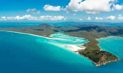 Stunning aerial view of crystal-clear turquoise waters, pristine white sandy beaches, and lush East Coast islands beneath a vibrant blue sky.