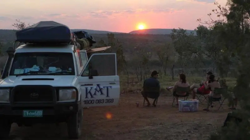 Travellers relax beside a 4WD van at sunset during their 10 Day Broome to Darwin Kimberley Adventure, immersed in nature’s beauty.