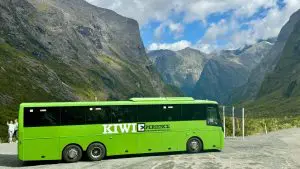 Image of Large green Kiwi Experience bus with the background of Milford sound