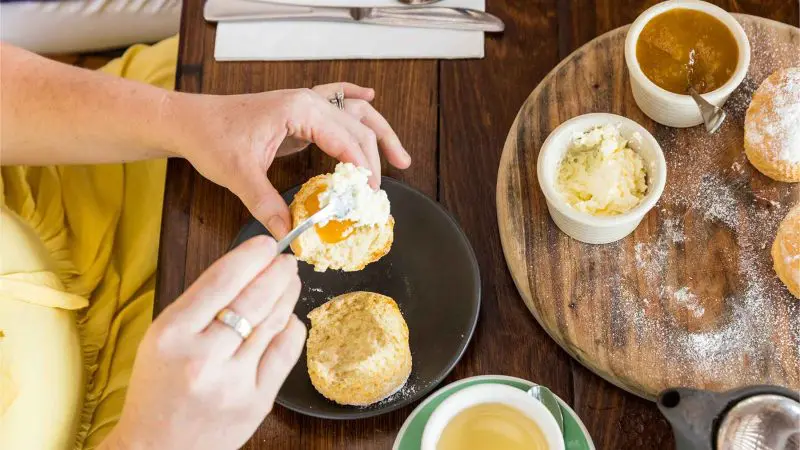 A person enjoys cream and jam on a scone during a CSHD Tour at a wooden table in Cairns City.