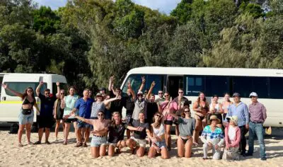 backpackers exploring K'gari at the beach with a bus in the background