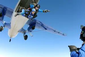 a skydiving instructor and tandem partner jumping out of an airplane with the plane in the background and blue skies