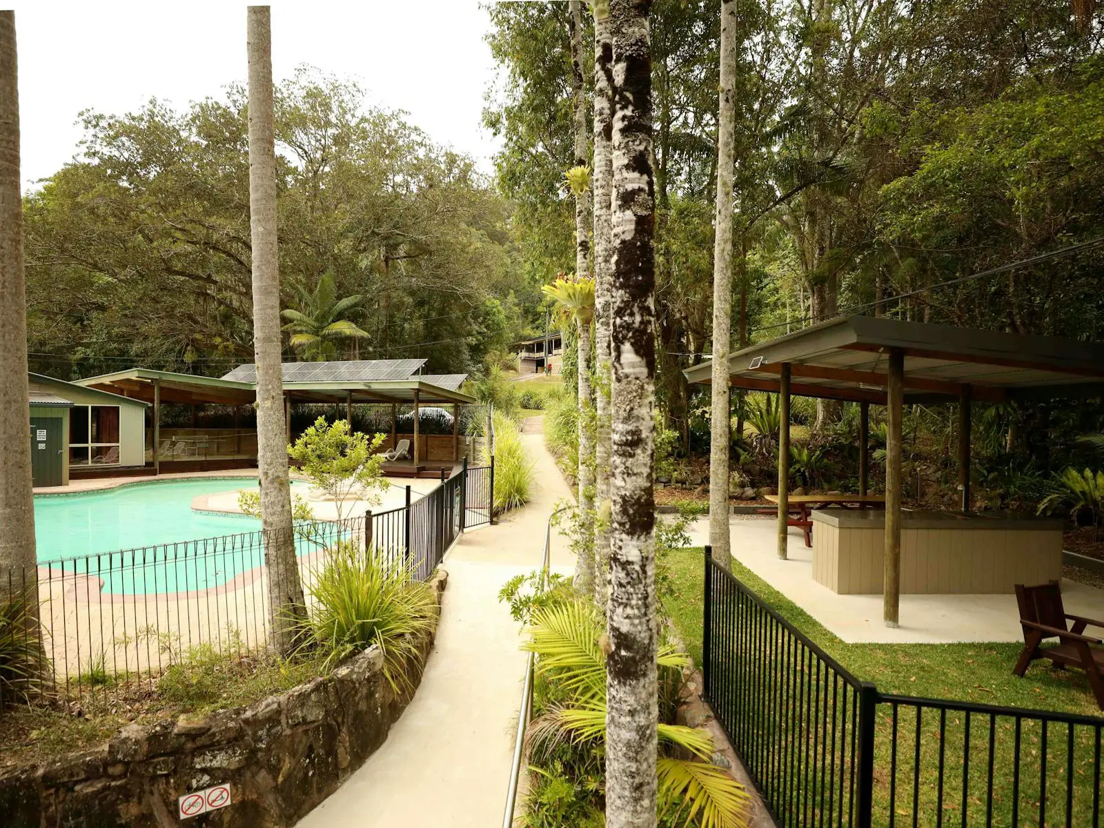Walkway of campsite with blue swimming pool on the left side and barbecues on the right side