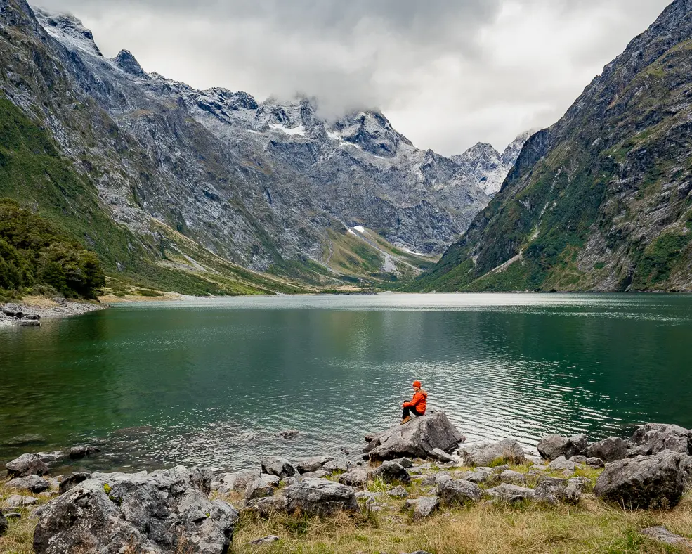 woman sitting on a rock infront of a lake with mountains on both sides of her