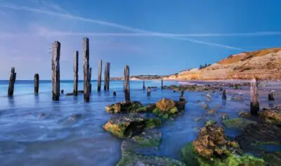 Beautiful sticks in the ocean sticking out of dark blue water with red rock in the background