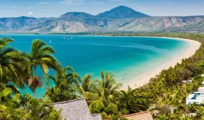bright blue ocean water with mountains in the back. palm trees and white sand along the coast