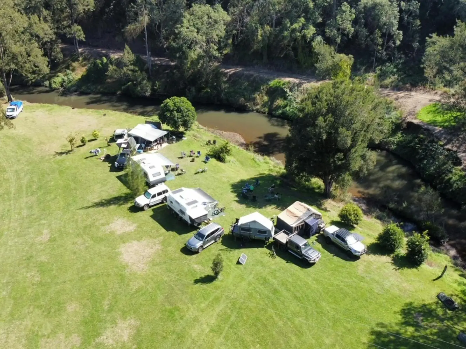 multiple camp setups right on the creekside. green grass and trees line the water