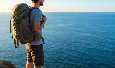 Image of male traveller on the top of a cliff by the Ocean carrying a small backpack